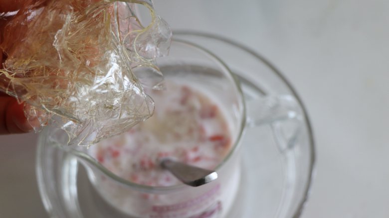 自制健康美味的草莓牛奶果冻,泡软的吉利丁片挤干水分，放到杯中，搅匀使其融化。