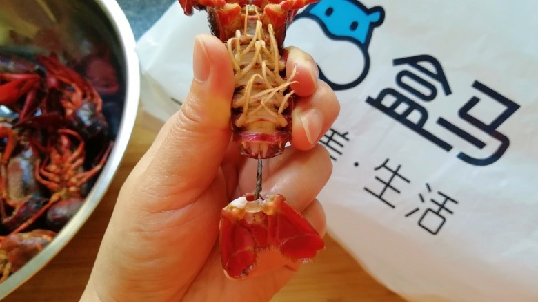 青花椒辣卤小龙虾,断生的小龙虾捞出晾一下，捏着小龙虾的尾巴最后一节，左右拧一下抽出虾线，如图。