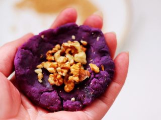 紫薯酸奶果仁芝麻饼,把紫薯面团分成6个大小一样的剂子，取一个剂子用手摁扁后，放入适量的果仁。