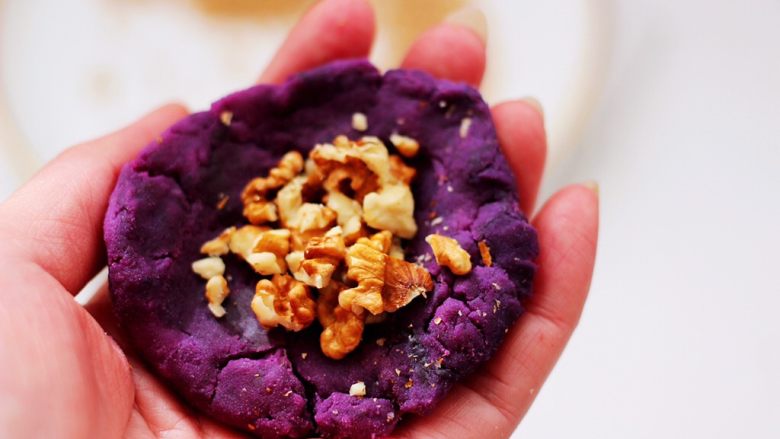 紫薯酸奶果仁芝麻饼,把紫薯面团分成6个大小一样的剂子，取一个剂子用手摁扁后，放入适量的果仁。