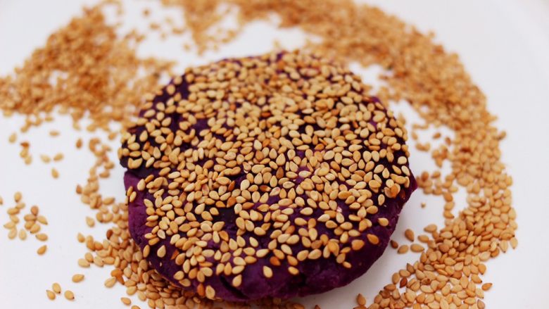 紫薯酸奶果仁芝麻饼,捏紧后揉圆再用手摁扁，面饼上面再蘸上白芝麻即可。