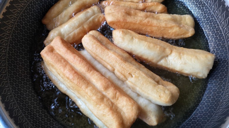 霜糖油条,炸的过程中用筷子不断的翻动，让油条可以受热均匀。