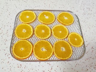缤纷水果干,甜橙表皮用盐搓洗干净，切成薄片，摆在烤网上。