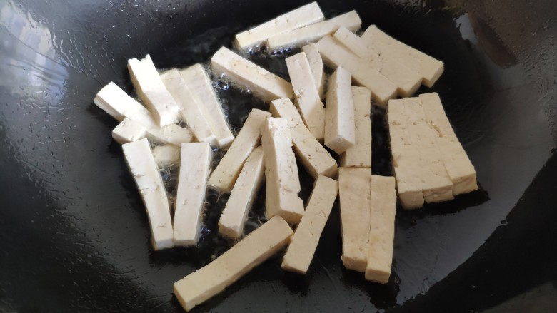 蒜薹炒豆腐,炒锅油热后，放入豆腐条。不要马上翻动它，把火调小一点，慢慢地来煎豆腐条。最好用不粘锅更容易些。