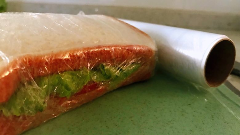 鸡胸肉三明治,用保鲜膜紧紧的裹起来，全部包裹完之后，拿刀从中间切开，此时，案板和刀特别重要了，为了避免细菌的交叉感染，生熟案板板和刀一定是分开的。