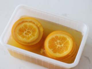 满满“一颗橙子”的香橙蛋糕卷,4. 煮好的橙片连同糖水一起装入保鲜盒，室温放凉后转入冷藏一夜。（不冷藏过夜也可以用，只是经过冷藏橙皮香味会更好）

