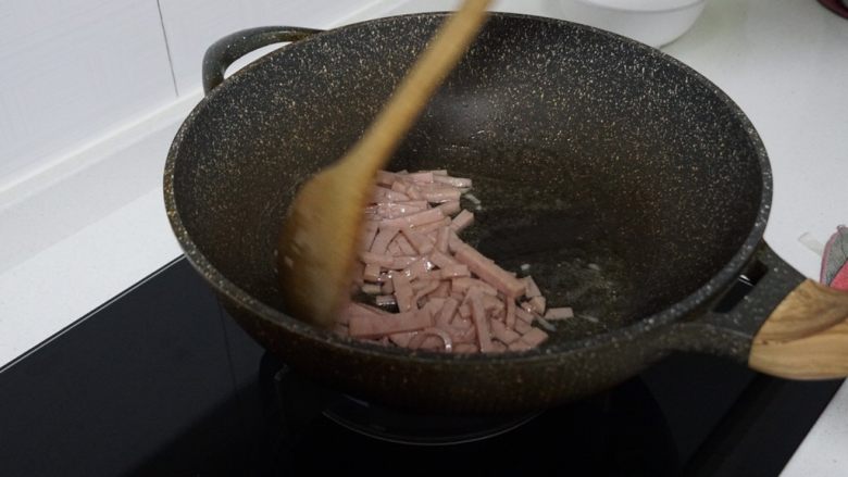 家常菜之卷心菜炒粉丝,将油锅预热后，开中火倒入少量油，放入火腿肉翻炒