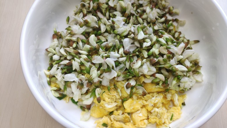 抱蛋槐花麦穗包,将鸡蛋碎和槐花以及韭菜一起放到大碗里。

