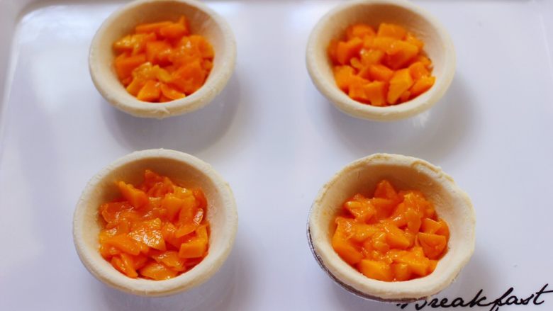 美味芒果酥,看见蛋挞皮软化以后，把切碎的芒果均匀的放到蛋挞皮里。