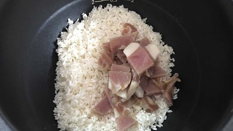  豌豆咸肉焖饭,把淘洗干净的糯米和咸肉一起放入电饭煲。