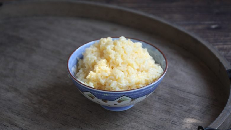 春日包菜饭便当,将米饭放在个较大的容器里，磕入一个鸡蛋，将鸡蛋和米饭抓匀备用。