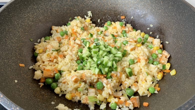 春日包菜饭便当,放入米饭，翻炒均匀，不停的翻炒，翻炒至米饭粒干爽，然后放入黄瓜丁，再次翻炒均匀。