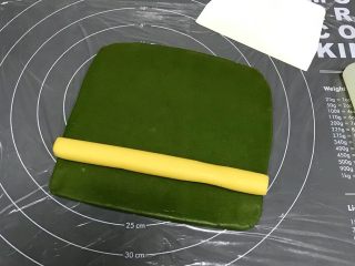 猕猴桃造型饼干,在硅胶垫上铺一张保鲜膜，把绿色面团擀成18*18cm的方形面片，放上原色长柱面团。