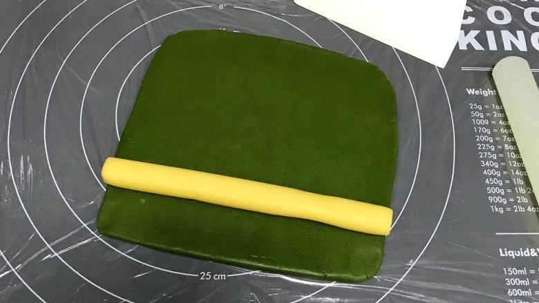 猕猴桃造型饼干,在硅胶垫上铺一张保鲜膜，把绿色面团擀成18*18cm的方形面片，放上原色长柱面团。