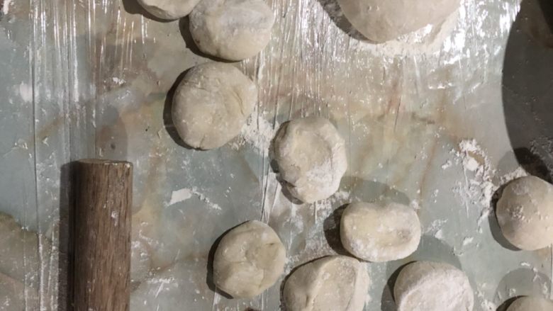 自制豆沙包,操作台铺保鲜膜充当揉面垫。面团分成两半，其中一半搓长，切成小剂子，用手按压一下，变成饼状。