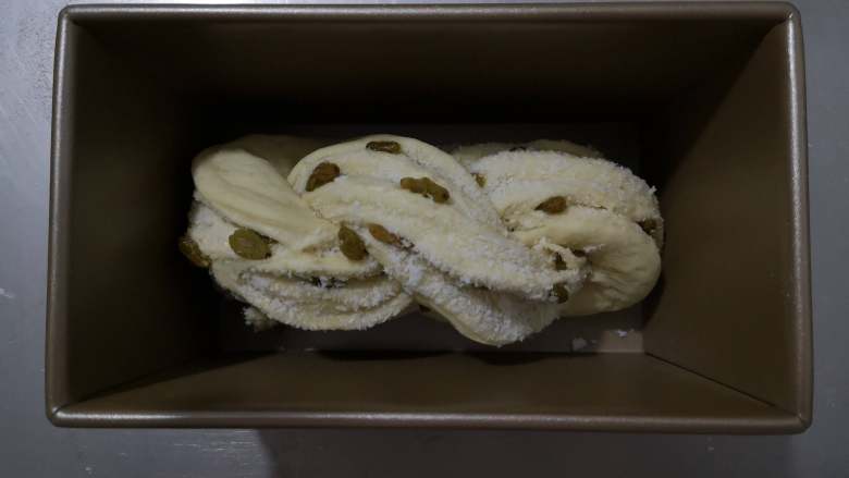 好吃又好看的椰蓉葡萄干吐司,将面包坯的两边往内折叠放入吐司盒中就可以进行二次发酵了。这次发酵我是放在烤箱里进行的，放了一碗热水在烤箱里加湿，发酵温度设为36度。