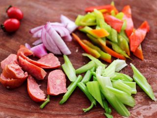 时蔬罗勒炒意面,把肉肠和洋葱，芹菜和青尖椒用刀切成片。