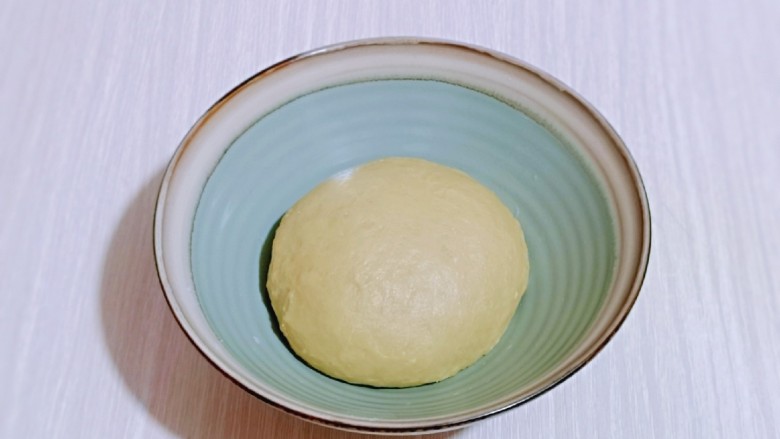 蜜豆喜饼～香甜松软,揉好的面团取出揉圆，盖上保鲜膜进行发酵。(面包机里直接发酵也可以)