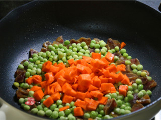 蔬菜腊肠饭,接着倒入胡萝卜粒，洗净的豌豆，大火翻炒片刻