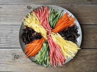 五彩拉皮,将黄瓜，胡萝卜，火腿片，蛋皮，焯熟的木耳切丝摆盘。