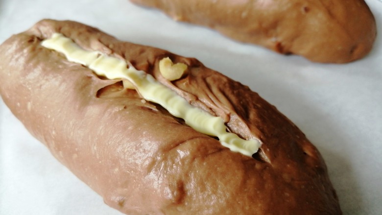 巧克力坚果面包,用面包割刀在面包表面割一条口子，把软化的黄油挤入。现在温度高，只需要把黄油放入裱花袋中，用手掌捂住一会儿，黄油就能软化了
