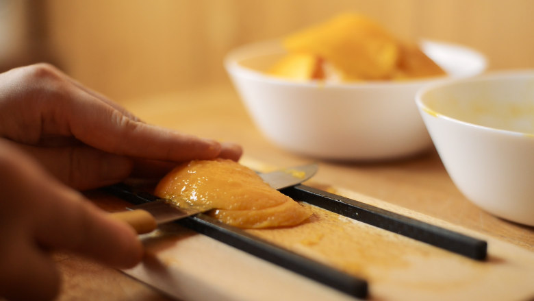 火龙很芒千层蛋糕,芒果片放在两根筷子中间，用水果刀片出2-3片厚度一致的芒果。