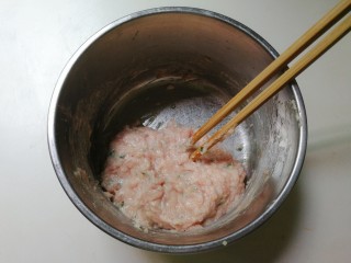 蚕豆仁汆汤丸子,再次顺时针搅拌至有粘性的肉糊，用筷子挑去肉糊摔打几下，摔出里面空气