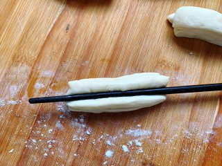 酵母版油条,用筷子在中间按压一下。盖上保鲜膜，醒发10分钟，让面起蜂窝，这样吃起来口感会更加暄软。