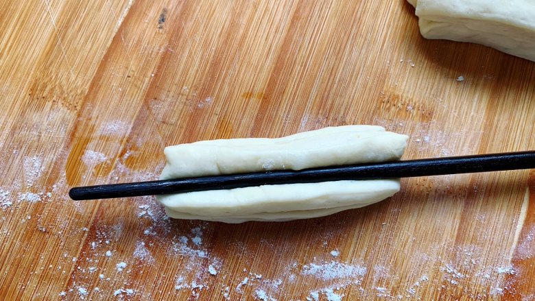 酵母版油条,用筷子在中间按压一下。盖上保鲜膜，醒发10分钟，让面起蜂窝，这样吃起来口感会更加暄软。