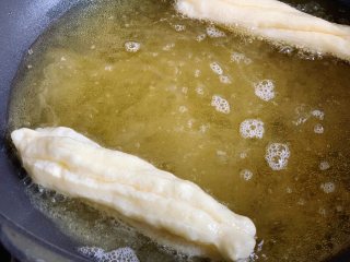 酵母版油条,锅内倒入适量玉米油，烧至7成热时，用手捏住油条胚头尾两端，轻轻拉长扭一下放入锅里。