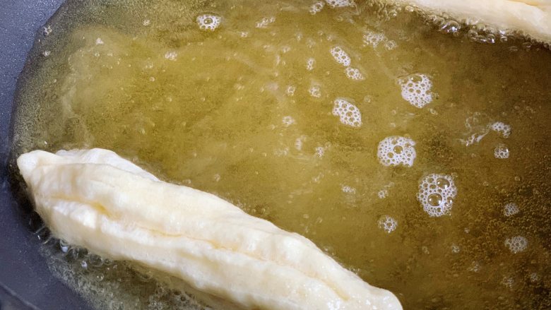 酵母版油条,锅内倒入适量玉米油，烧至7成热时，用手捏住油条胚头尾两端，轻轻拉长扭一下放入锅里。