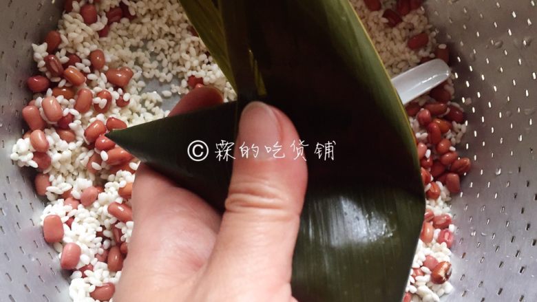 赤豆三角粽,把另一边的粽叶翻过来，盖住斗里的糯米，大拇指和食指捏紧粽身的的左右两端，成为一个三角形。