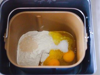 胶东喜饼,把称重的中筋面粉和白糖，两个鸡蛋打散放入面包桶里，倒入花生油和酵母，启动面包机的和面模式开始和面。