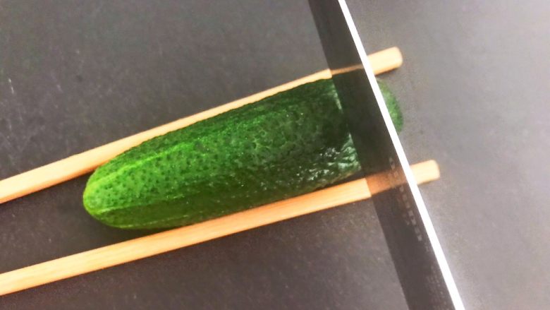 风味酱香乳瓜,取一个小乳瓜，在乳瓜的两侧放上筷子，用刀切成连刀片
