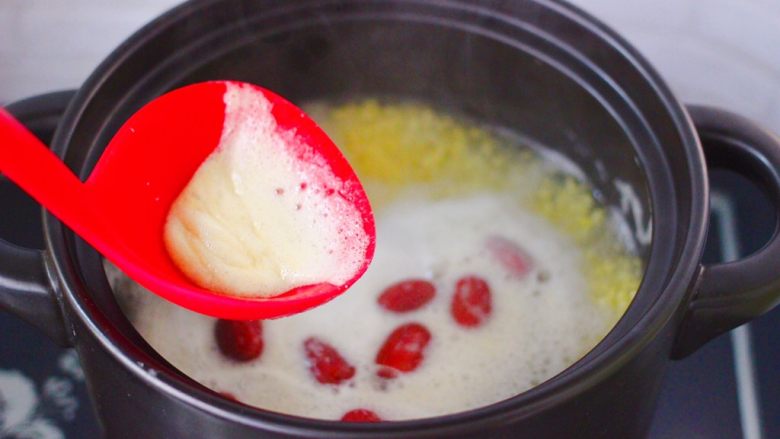 红薯百合红枣小米粥,用勺子撇去上面的浮末。