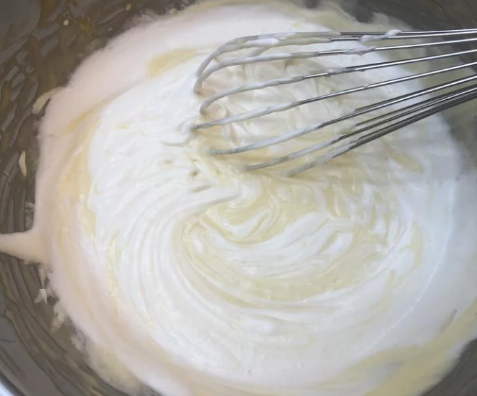 百香芒果双层生乳酪蛋糕（免烤箱）,先挖取一半的鲜奶油加入步骤6锅中拌匀后，再加入剩下的鲜奶油轻柔拌匀。※加入鲜奶油时必需确认奶油乳酪锅已恢復常温，否则鲜奶油会溶化。