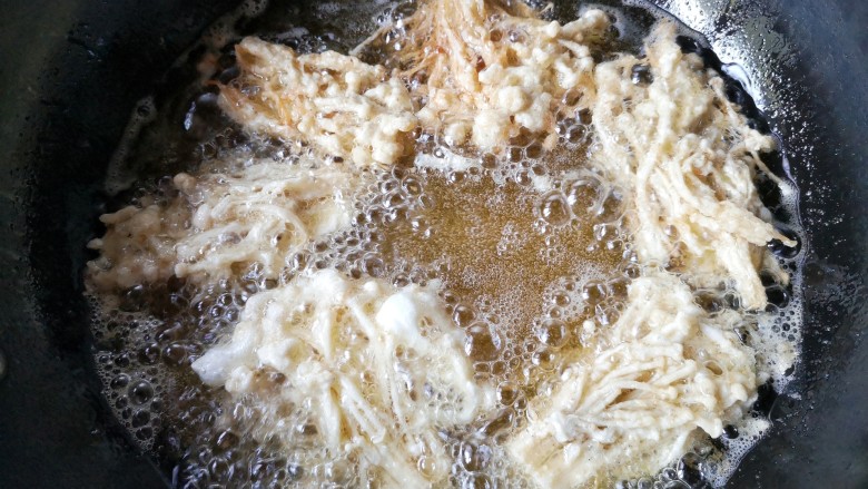 椒盐金针菇,锅中宽油，烧至5-6成热，将包裹裹炸粉的金针菇下锅。