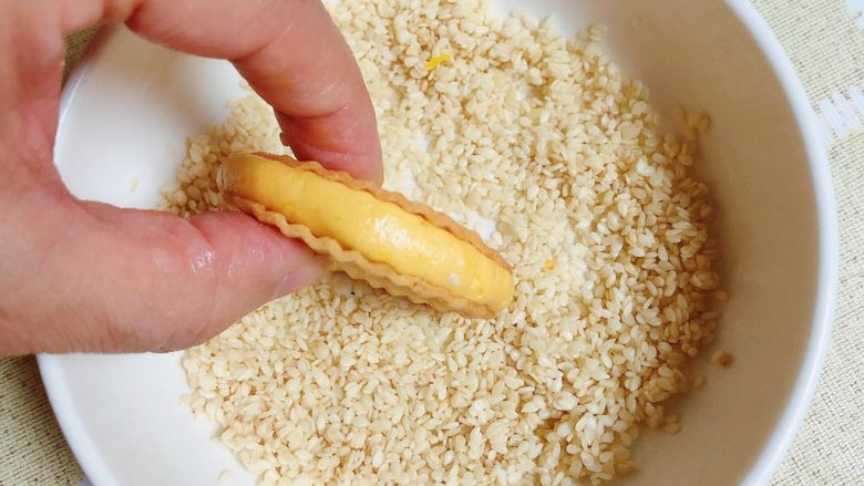 南瓜糯米薯片饼,将夹心饼在白芝麻碗中滚一下，粘上一圈白芝麻。