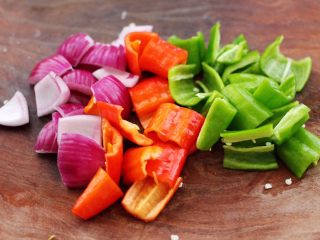 时蔬孜然烤鸡肉串,把洋葱和青红椒洗净后，用刀切片方片。