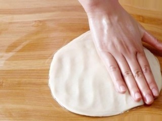 香蕉飞饼卷,取出面团，放在案板上，用手掌按扁，手掌根压着面饼向四周拖开，形成薄饼状。