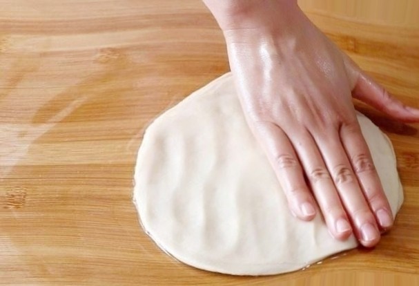 香蕉飞饼卷,取出面团，放在案板上，用手掌按扁，手掌根压着面饼向四周拖开，形成薄饼状。