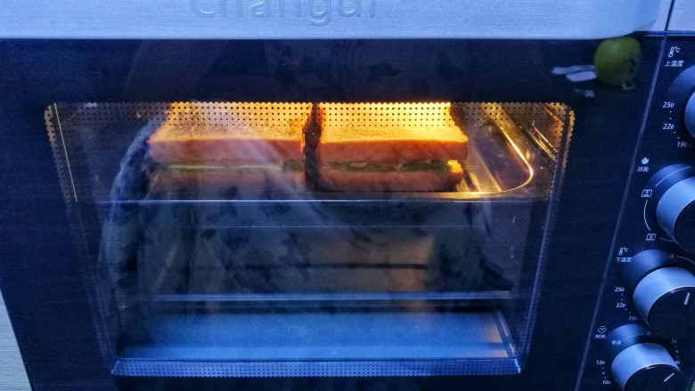牛油果鸡蛋火腿三明治,放入烤盘，推入预热好的烤箱，180度烤5分钟。放温然后用保鲜膜裹好三明治，从中间切半即可。