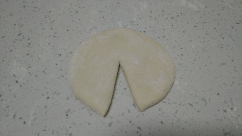 寿桃馒头,取一个剂子压扁，用擀面杖擀成薄片，从中间切开到一边。