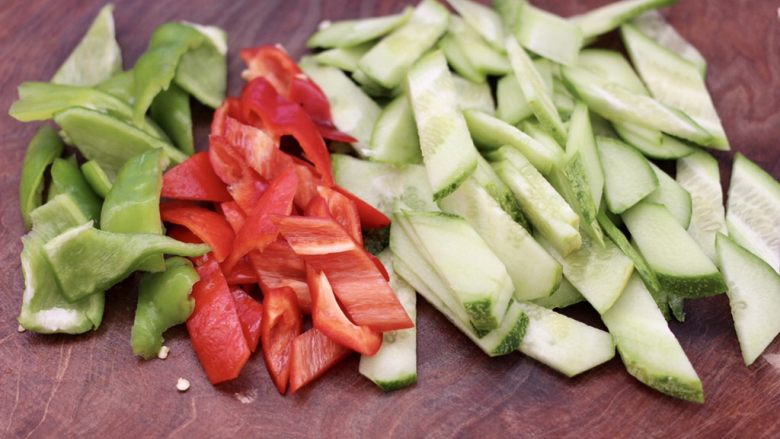 黄瓜双椒炒肉便当,把洗净的黄瓜，用刀切成菱形薄片，青红尖椒切片。