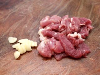 黄瓜双椒炒肉便当,把猪肉洗净后，用刀切成薄片，大蒜去皮后，用刀切成薄片。