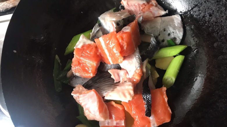 姜炒三文鱼头,葱姜蒜炒香后下沥干的三文鱼。翻炒2分钟左右，炒到鱼肉变色。