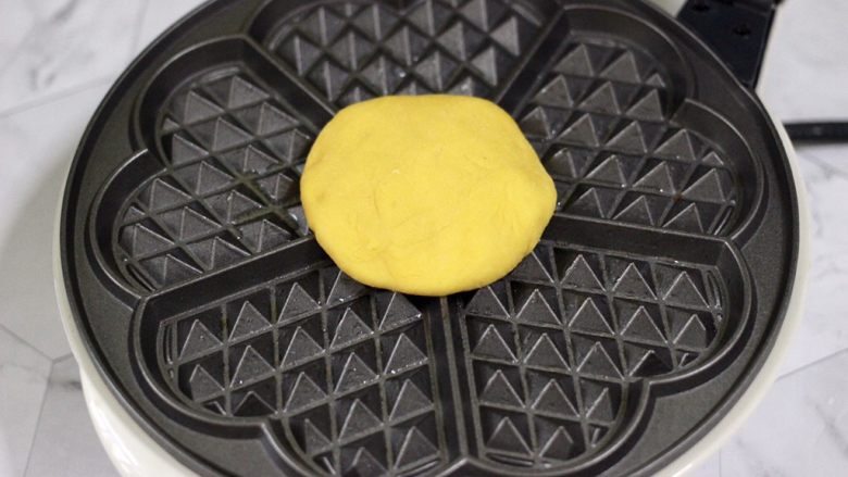 南瓜酸奶华夫饼,华夫饼机提前预热后，刷上薄薄的一层黄油，把摁扁的面饼放入机器里，盖上盖子开始烙制。