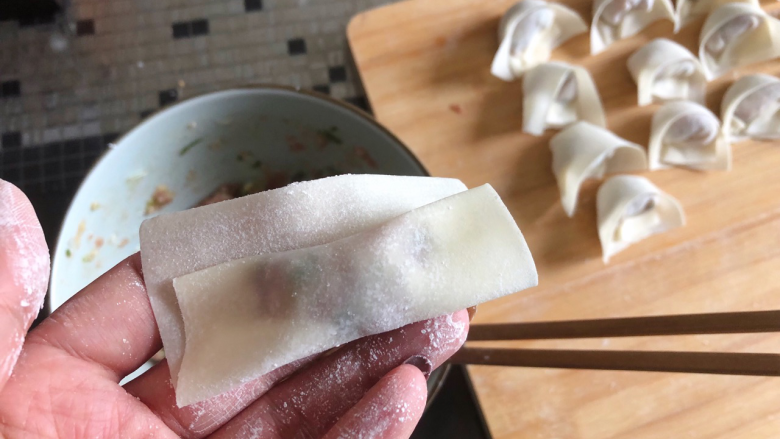 鲜香馄饨,把肉馅从底部慢慢卷起来，留一指空的距离，用筷子沾一点水抹在一侧。