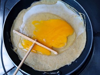 杂粮煎饼,待煎饼周围开始翘起时，在煎饼上打上个鸡蛋，用推子将鸡蛋敲散，均匀铺满煎饼上。