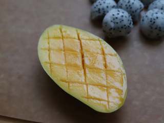 酸奶水果挞,芒果沿果核的走向切半个出来，用刀在芒果上划出菱形的花纹，注意不要切段皮，然后顺势将芒果底部往上推，芒果就全露出来了。